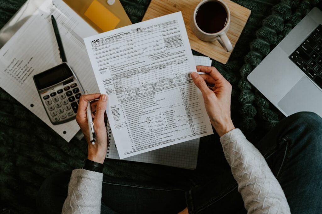 Hands holding tax forms with calculator and laptop.